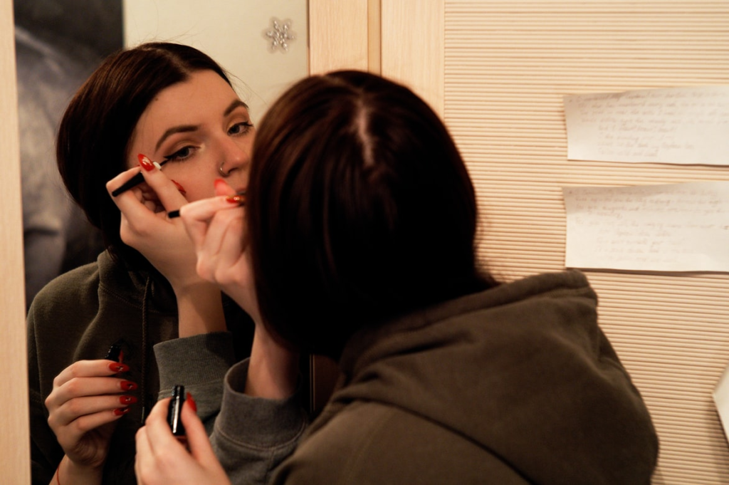 A woman applying makeup in front of a mirror.