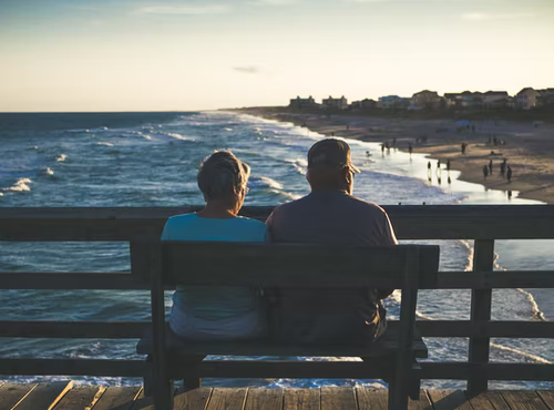 An old couple sitting on a bench looking at the sea