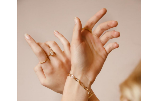 A woman wearing a gold bracelet and rings.