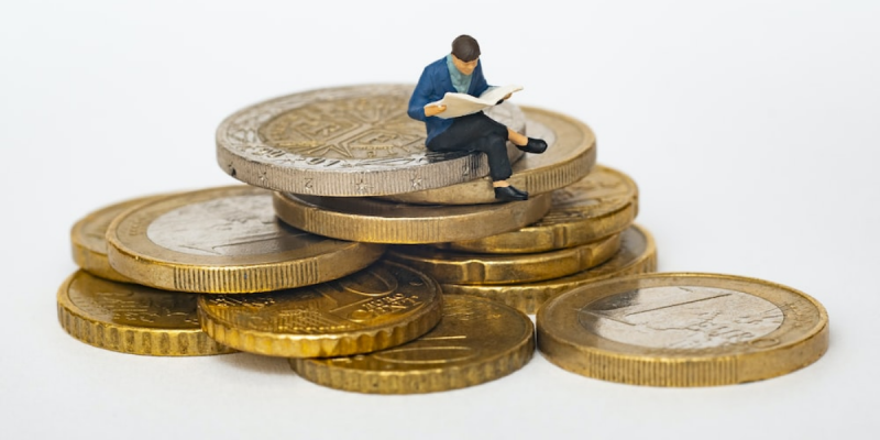 Miniature person sitting on gold coins