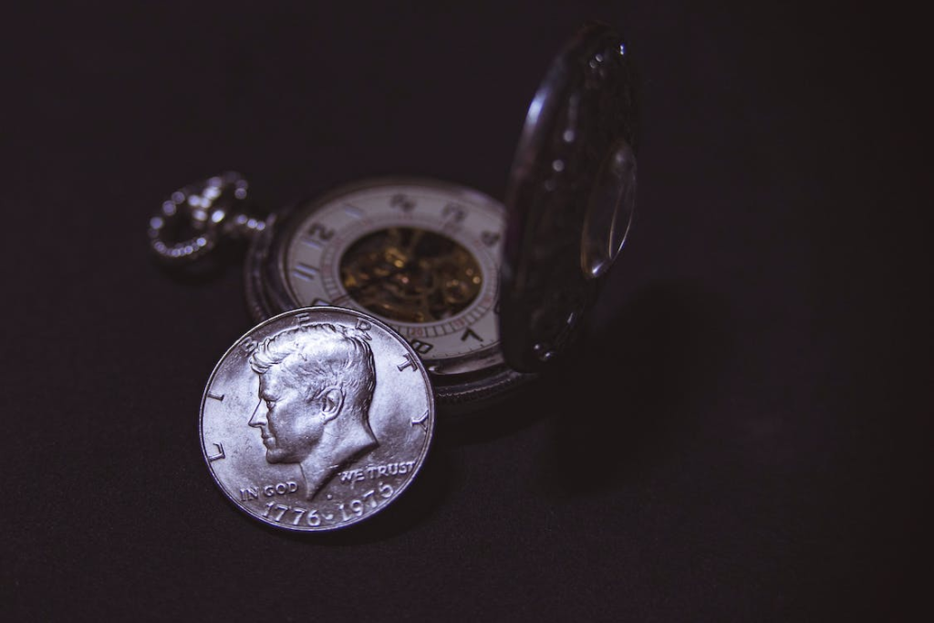 A photo of a silver pocket watch and a coin