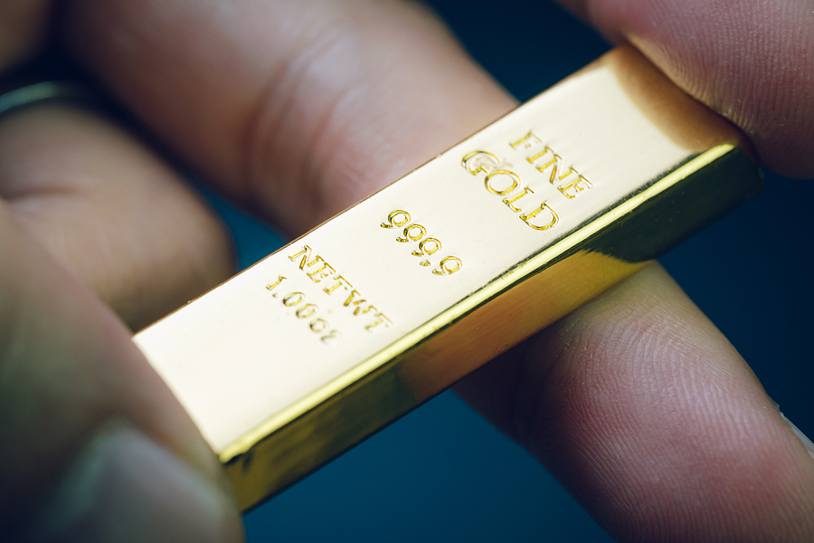 Hand holding gold bar as investment asset or safe haven on financial crisis, shinny ingot or bullion studio shot with dark background.